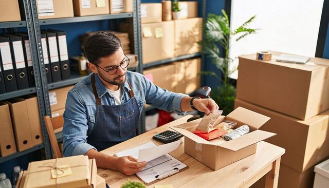 Small Business Owner Packing Orders at Desk with Cardboard Boxes and Invoices