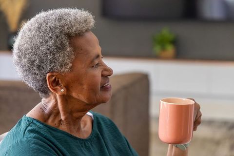 Senior african american woman holding peach mug relaxing at home on sofa