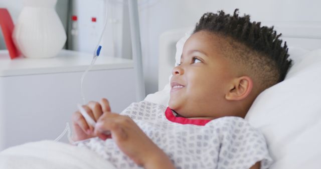 Happy african american boy patient lying in bed at hospital smiling. Medicine, healthcare, lifestyle and hospital concept.