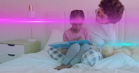 Mother and daughter reading tablet in cozy bedtime moment with teddy bear and plaid pajamas