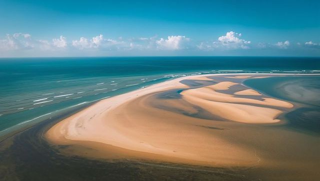 Crescent sandbar curving seaward with tidal channels over turquoise ocean aerial drone