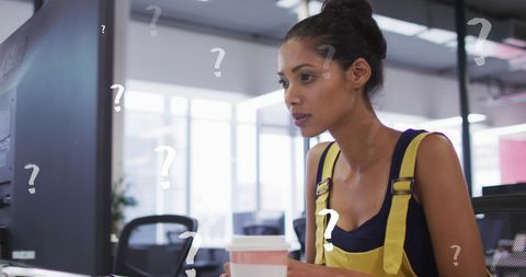 Confused woman in office working on computer with question marks
