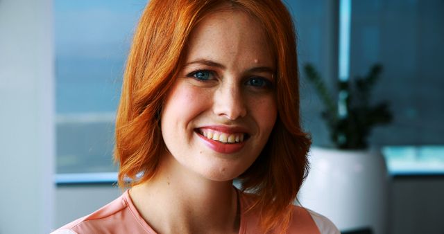 Smiling redheaded woman in a modern office setting. Ideal for business websites, professional networking, workplace inclusion campaigns, and corporate training materials showing positive and confident employees.