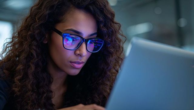 Focused Woman Coder with Glasses Working on Laptop in Modern Office