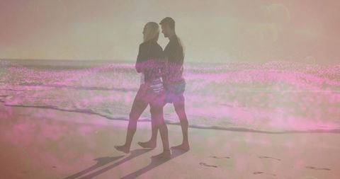 Couple strolling along beach at sunset with romantic glow
