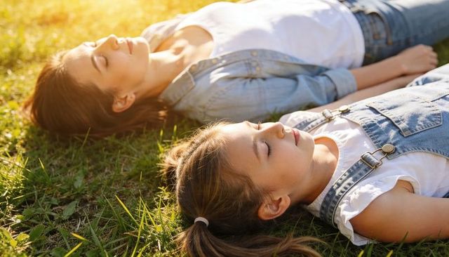 Mother and daughter relaxing on grass soaking golden sunlight peaceful bonding moment