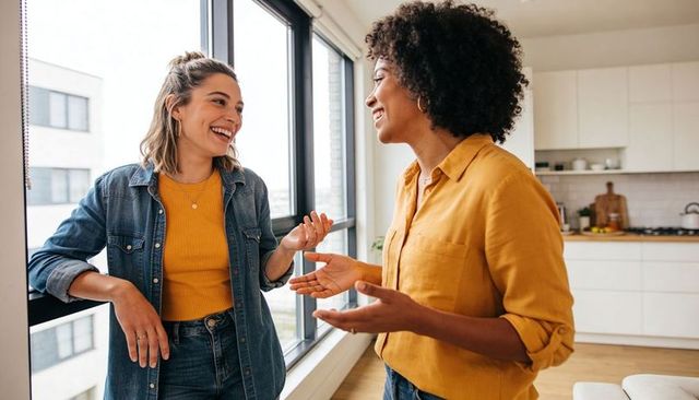 Friends chatting in bright urban kitchen wearing mustard tops and denim jacket smiling