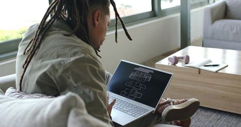 African american man reviewing architectural floor plan on laptop in modern living room