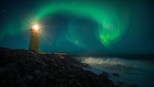Lighthouse Casting Starburst Beacon under Northern Lights over Rocky Coastal Waves at Night