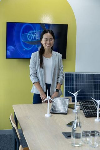 Asian sustainability engineer presenting wind turbine and solar panel prototypes in office