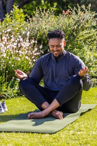 Man meditating outdoors on yoga mat in garden practicing mindfulness, relaxation, wellness