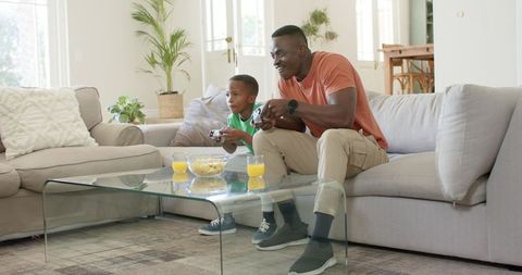 African american father and son playing video games on cozy living room sofa
