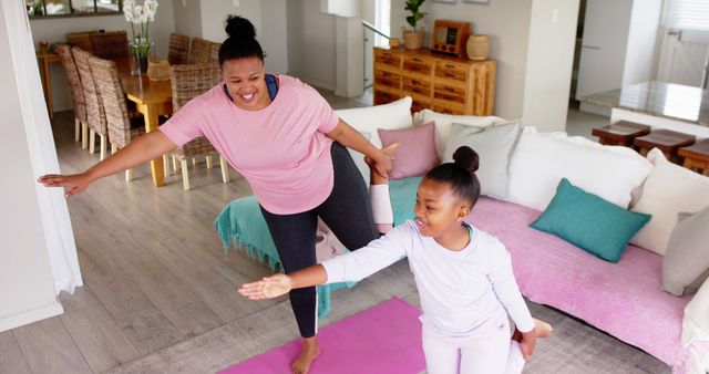 Mother and daughter practicing yoga at home together, focusing on family bonding and healthy living. They are smiling and enjoying their time, suggesting a joyful family activity in a cozy living room setting. Useful for illustrating family fitness, home workout routines, and promoting a balanced lifestyle.
