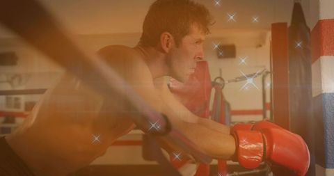 Male boxer leaning on ring ropes taking breath and refocusing between rounds with moody light
