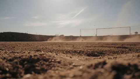 Low-angle arid dirt field stretching to horizon with dusty goalposts and gritty texture