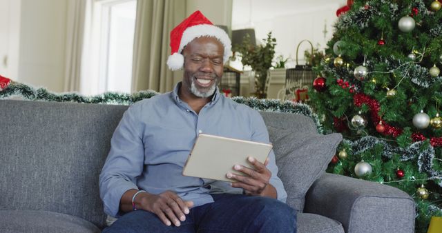 Happy Man in Santa Hat Using Tablet Next to Christmas Tree - Download Free Stock Images Pikwizard.com