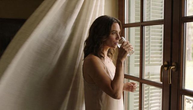 Woman sipping water, gazing through french doors, curtain flowing in soft morning light