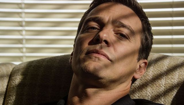 Man reclining in armchair catching striped sunlight through venetian blinds