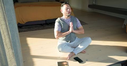 Asian Man Practicing Meditation Next to Bed with Sunlit Serenity