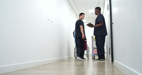 Medical staff discussing patient care in hospital corridor, pushing wheelchair and cart