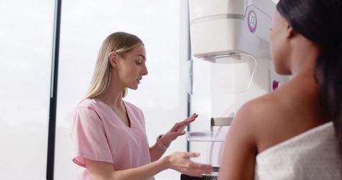 Female radiologic technologist in pink scrubs preparing patient for mammogram in clinic