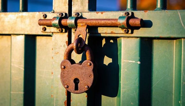 Rusted heart-shaped padlock securing weathered green metal gate in sunlight