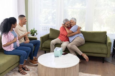 Senior couple hugging on sofa while adult children visit in multigenerational living room