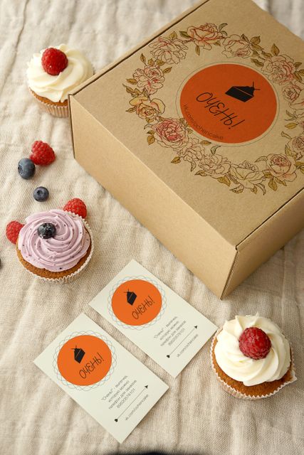 Beautiful display of gourmet cupcakes in various flavors, boxed and accompanied by business cards on a linen background. Ideal for showcasing artisanal bakery branding, dessert promotions, or packaging design concepts.