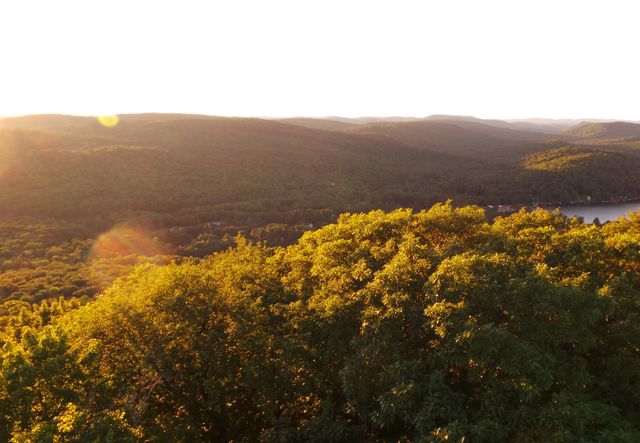 Sunset casting a warm glow over forested hills with a scenic overlook. Ideal for nature-themed prints, travel websites, and outdoor activity promotions. Suitable for background images in presentations or relaxation content.