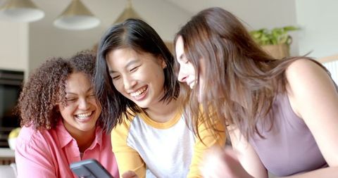 Diverse Friends Laughing Together Facing Smartphone on Sofa