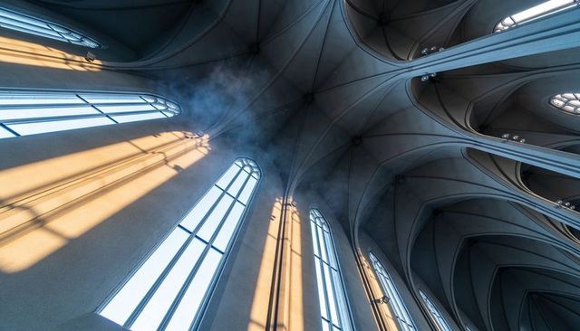 Sunbeams streaming through arched clerestory windows casting diagonal light across gothic vaults