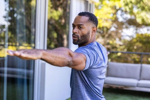 Mature african american man stretching in warrior ii yoga pose on sunny balcony fitness