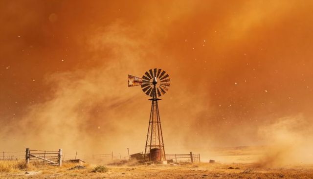 Spinning windpump tower turning rotor amid orange dust haze on arid rural plain