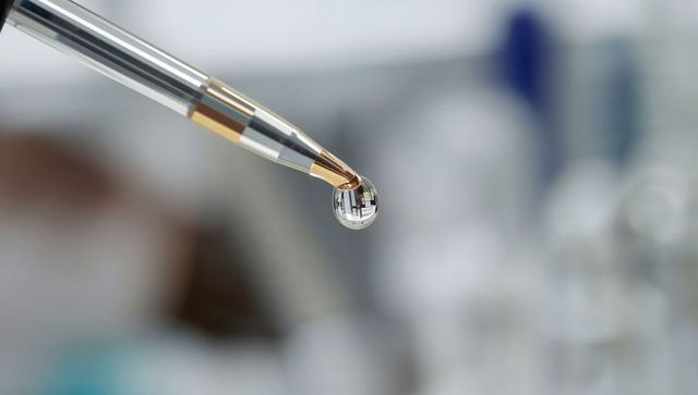 Dripping pipette tip forming amber droplet over lab bench macro scientific close-up