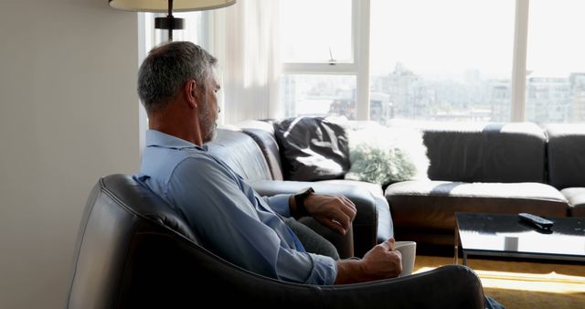 Man Relaxing on Couch Holding Coffee Mug in Modern Sunlit Living Room - Download Free Stock Images Pikwizard.com