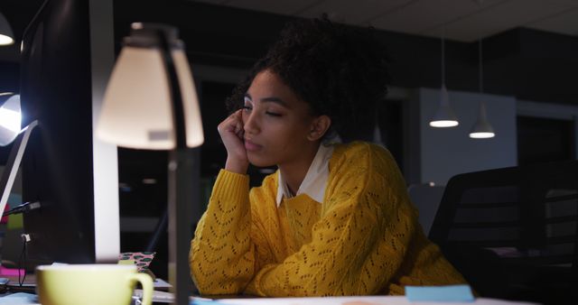 The woman, appearing exhausted, leans on the desk while working on the computer. Ideal for use in articles or advertisements about work-life balance, corporate duties, overtime work, or burnout. Useful for blogs discussing productivity challenges and the importance of taking breaks.