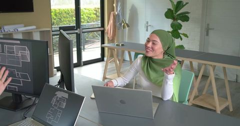 Muslim woman collaborating with coworker on architectural floor plans in design studio