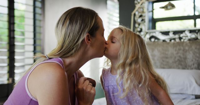 Caucasian mother and daughter kissing in bedroom. Lifestyle, childhood, family, togetherness and domestic life, unaltered.