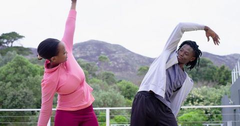 African American Couple Stretching Together on Balcony Overlooking Green Hills