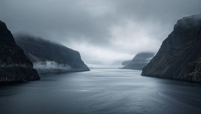 Misty fjord channel threading between steep cliffs with low fog shrouding coastal canyon