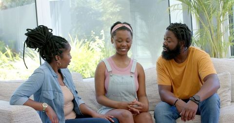 African family having supportive talk with teen daughter on bright living room sofa