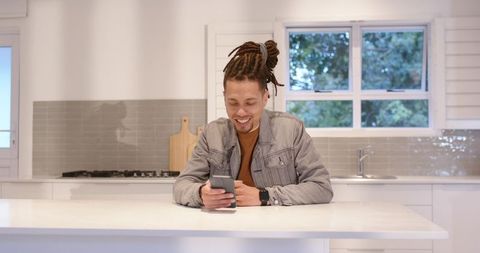 Young man checking smartphone and smartwatch while leaning on modern white kitchen island