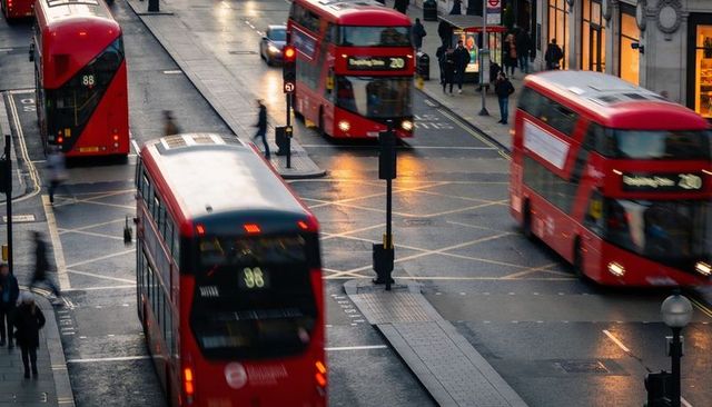 Red double-decker buses moving through london intersection evening wet street reflections