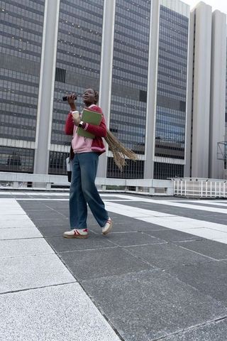 African american student walking on urban rooftop plaza holding notebook and phone