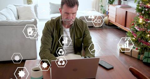 Mature man working from home with eco analytics overlay, laptop and Christmas decor