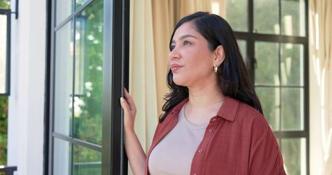 Woman gazing through black-framed glass door at garden, relaxed home moment