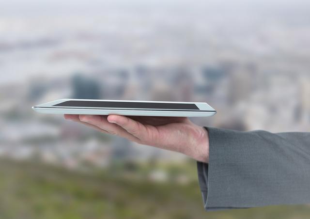 Digital composite of Hand with tablet against blurry skyline