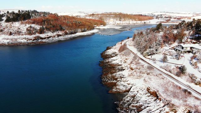 Aerial shot capturing serene snowy landscape along a river during winter. Ideal for use in seasonal promotions, nature photography collections, travel guides, and holiday-themed content.