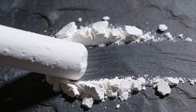 Crushed white chalk on dark slate closeup showing texture, powder lines, studio lighting