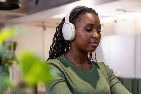 African american woman with white headphones working calmly in modern kitchenette coworking